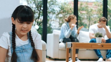 Stresli ve mutsuz genç kız köşeye kıvrılıp kulaklarını kapatarak arka planda ebeveyninin tartışmasını engelliyor. Evde aile içi şiddet ve travmatik çocukluk depresyona dönüşür. Eşzamanlama