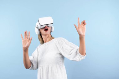 Mutlu kadın VR gözlüklerine bakıp mavi arka planda dururken şaşırdı ya da heyecanlandı. Beyaz pijamalı beyaz bir kız metaevrene bağlanmak için görsel gerçeklik gözlüğü kullanıyor. Kısıtlanma.