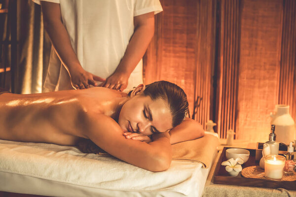 Caucasian woman customer enjoying relaxing anti-stress spa massage and pampering with beauty skin recreation leisure in warm candle lighting ambient salon spa at luxury resort or hotel. Quiescent