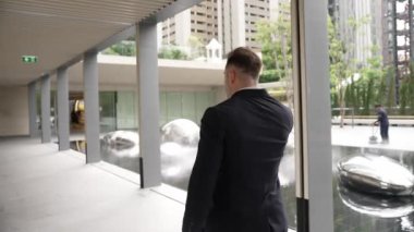 Modern koridorda yürürken telefonla konuşan mutlu yöneticinin arka görüntüsü. Akıllı patron yeşil şehirde yürürken finansal strateji planlamak için pazarlama ekibini arayarak telefonu kullanıyor. Urbane.