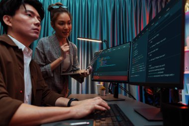 Modern ofisteki neon ışık odasında bilgi ağını gösteren dizüstü bilgisayarla iki ekranda veri çalıştıran akıllı web sitesi geliştirme kodlayıcı sistemini tartışan IT geliştiricilerinin ciddiyeti. İnfobahn.