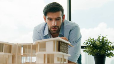 Akıllı Kafkasyalı mühendis veya proje yöneticisi ölçüm, teftiş, panorama penceresinin yanında, gökdelen manzaralı ev modeline bakın. Yönetici tasarım evi inşaatı. İzleme