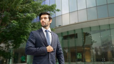 Binanın önünde duran yakışıklı beyaz bir iş adamı. Kameraya havalı poz verirken etrafa bakınan yetenekli bir yatırımcı. Akıllı proje yöneticisi resmi takım elbise giyiyor. Vizyon ve profesyonellik. Sevinçli..