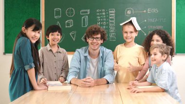 Profesyonel Kafkas öğretmeni ve çeşitli öğrenciler kameraya bakarken mutlu çocuk başparmak gösteriyor. Sınıfın önünde dururken gülümseyen bir grup çok kültürlü çocuk. Eğitim. Pedagoji.