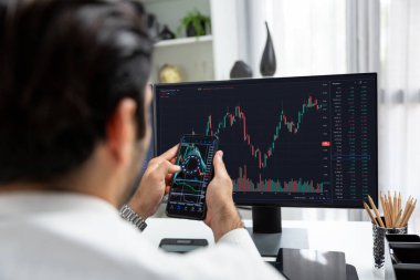 Akıllı telefondan akıllı telefon arayan tüccar işadamı, bilgisayardaki dinamik borsa yatırım ekranını analiz ediyor ve modern merkez ofisteki en kârlı finansal teknoloji pazarına yatırım yapıyor. Tahmin et..