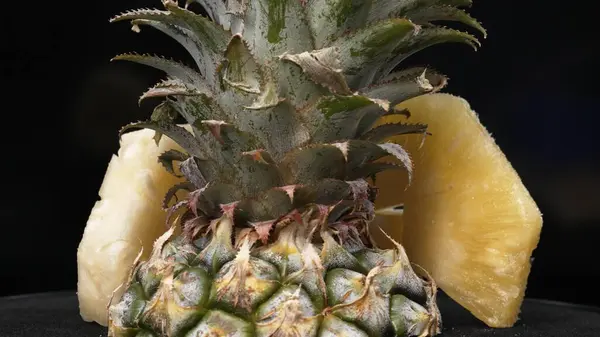 stock image Close up video of fresh pineapple with slice of peel pineapple insert with separated black background. The rough and waxy rind, boasting a crown of spiky green leaves, Food photography. Comestible.