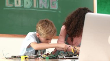 Kök sınıftaki ana tahtayı tamir ederken karatahtadaki dizüstü bilgisayara bakan çeşitli zeki öğrenciler. Bir grup yetenekli çocuk elektronik makineleri öğreniyor ve öğreniyor. Pedagoji.