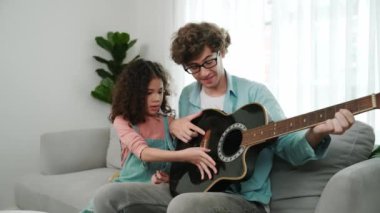 Beyaz bir baba, tatlı kızına koltukta otururken gitar çalmayı öğretiyor. Müzik öğrenirken babasına gitar çalarken bakan tatlı öğrenci kız. Aile eğlence konsepti. Pedagoji.