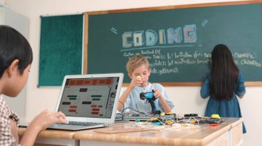 Kafkas arkadaşı STEM sınıfında elektrik panosunu tamir ederken Asyalı çocuk kodlama programı. Enerjik öğrenci kodlama mühendisliği komut yazarken ve yapay zeka yazılımını programlarken tahtada duruyor. Pedagoji.