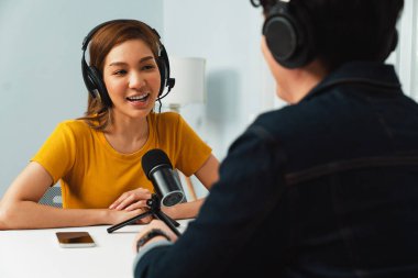 Gülümseyen radyo etkili sunucusu kulaklık takıyor kadın konuşmacı ile röportaj yapıyor sosyal medya internet sitesinden dinleyicilere bilgi paylaşıyor stüdyo kaydında sabah canlı yayın kanalı. İnfobahn.