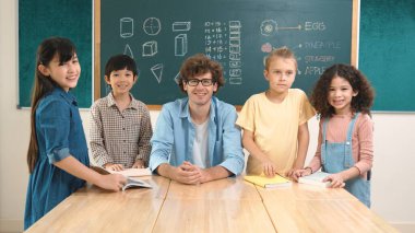 Profesyonel Kafkas öğretmeni ve çeşitli öğrenciler kameraya bakarken mutlu okul çocuğu gülümsüyor. Sınıfın önünde dururken gülümseyen bir grup çok kültürlü çocuk. Eğitim. Pedagoji.