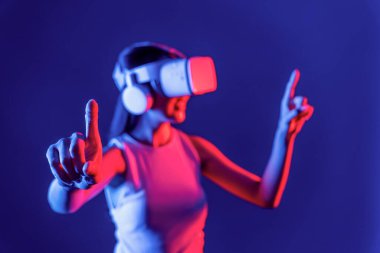 Siberpunk neon ışıklı cihazlarla çevrili zeki bir kadın metaevrene bağlı VR kulaklık takıyor, gelecekçi siber uzay teknolojisi. Sanal objeyi işaret eden bir kadın. Halüsinasyon.
