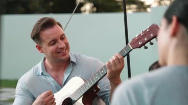 Baba gitar çalarken anne ve kız birlikte kampta oturuyorlar. Ebeveynler, genç nesil çapraz kuşak farklılıklarıyla zaman geçirmek için açık hava kamp aktivitelerini kullanıyorlar. Uyumsuzluk.