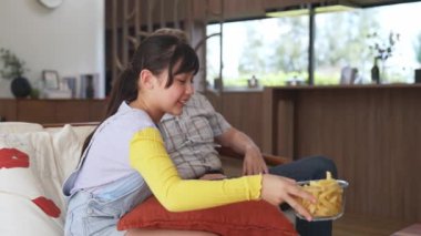Grandfather and granddaughter eat french fries watch interesting entertainment on TV. Senior use technology communicate with young generation cross generation gap strengthen family bond. Divergence.