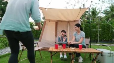 Aile hep birlikte bahçedeki kampta oturup yemek yiyor. Ebeveynler, genç nesil arasında iletişim kurmak ve zaman geçirmek için açık hava kamp faaliyetlerini kullanıyorlar. Uyumsuzluk.