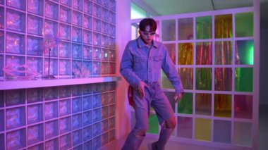Gece kulübünde kameraya bakarken güneş gözlüklü Asyalı dansçı serbest dans ediyor. Mutlu sokak dansçısı dans ediyor ve renkli parlak neon ışığı ya da yol gösteren ışıkla ayak seslerini gösteriyor. Mutluluk.