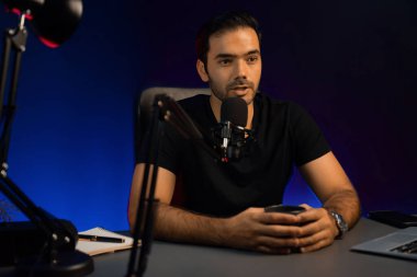 Yayıncı elinde kahve fincanıyla hayran kulübü dinleyicisiyle konuşuyor, canlı yayında neon ışık stüdyosundaki yaratıcı pozitif düşünce konseptiyle ilgili finansal sorunları tartışıyor. Tahmin et..