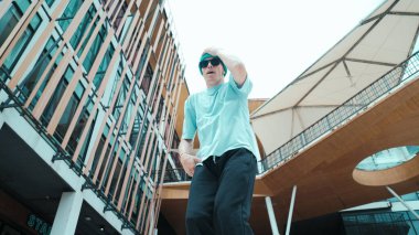 Kameraya bakan beyaz sokak dansçısının portresi. Genç, çekici bir adam, modern alışveriş merkezinde hip hop gösterisi yapıyor. Düşük açı. Serbest stil dansı. Açık hava sporu 2024. Hiphop.