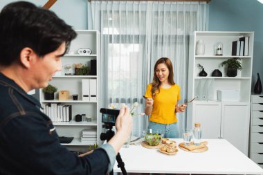 Asyalı güzel kadın yemek uzmanı blog yazarı akıllı kameramanın sosyal medya kavramında canlı yayında kaydettiği canlı yayında salatanın nasıl kolay pişirileceğini öğretiyor. İnfobahn.