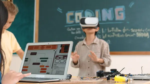 stock image Asian boy wearing VR headset to enter metaworld at table with electronic board while girl coding system. Group of diverse student working together to develop program and writing engineering code