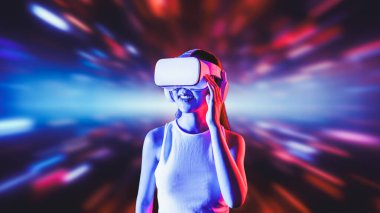 Zeki bir kadın, metaevreni birbirine bağlayan VR kulaklık takan neon ışıklarla çevrili duruyor. Gelecekteki siber uzay topluluğu teknolojisi. Uzaklara bakan zarif bir kadın ve tatmin edici bir şekilde gülümsüyor. Halüsinasyon.