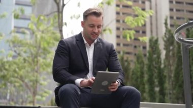 Green City 'de otururken tablet üzerinde çalışan iş adamlarına yakın durun. Düşük açılı kamera, yönetici tabletini kullanarak uzaktan çalışırken finansal veri analizini tarıyor. Urbane.