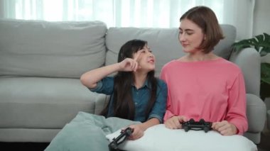 Aktif kız ve Kafkas anne birlikte oyun oynarken ve oturma odasında kanepenin yanında otururken poz veriyorlar. Çekici kız ve anne battaniyeyle joystick tutarken birlikte vakit geçiriyorlar. Pedagoji.