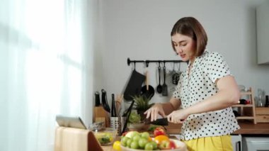 Kafkasyalı anne, modern mutfakta dizüstü bilgisayarda yemek tarifine bakarken salata yapmak için yemek hazırlıyor. Yetenekli ev bekçisi taze sebze kullanarak kahvaltı hazırlıyor. Pedagoji.