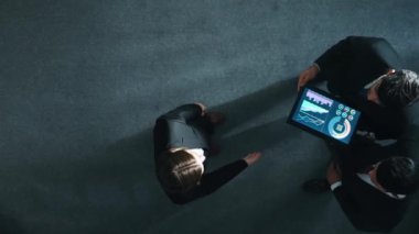 Zeki yöneticinin çeşitli takımlarla tokalaştığı ve tabletteki finansal verileri analiz ettiği yukarıdan aşağıya hava görüntüsü. Kadın lider bir anlaşma yaparak gruba katılıyor ve pazarlama stratejisini paylaşıyor. Müdürlük.