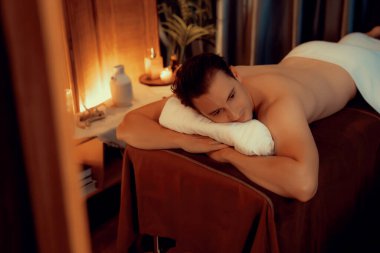 Beyaz erkek müşteri stres önleyici spa masajının keyfini çıkarıyor ve lüks otel ya da oteldeki ortam kaplıcalarında sıcak mum ışığında güzellik teniyle eğleniyor. Sessiz.