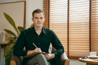 Psikiyatri ofisinde ya da terapi odasında koltukta oturan mutlu ve gülümseyen erkek psikolog portresi. Arkadaş canlısı ve profesyonel ruh sağlığı danışmanı ve terapisti. Açılıyor