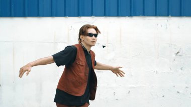 Beyaz arka planda break dans pratiği yapan yakışıklı bir sokak dansçısı. Hip hop tarzı giyinen sporcu, mavi arka planlı bir sokakta müzik eşliğinde ayak sesleri çıkarıyor. Açık hava sporu 2024 hiphop..