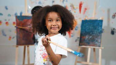 Öğrencinin arkasında resim çizerken elinde fırça tutan Afrikalı tatlı bir kız. Çok kültürlü çocuklar sanat dersine katılırken güzel öğrenciler kameraya bakıyor. Yaratıcı aktivite konsepti. Etkinlik.