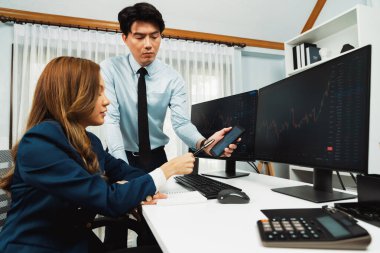 Gülümseyen işadamı cep telefonundaki dinamik borsa verilerini, iç ofisindeki internet sitesi uygulamasını analiz etmek için not yazan kadınlara gösteriyor. İnfobahn.