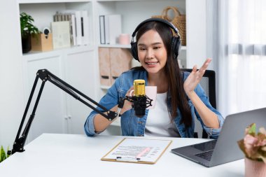 Sosyal medyada kulaklıkla canlı yayın yapan Asyalı sunucu modern stüdyoda yaşam koçluğu veya pazarlama dinleyicilerini selamlıyor. Taktik.