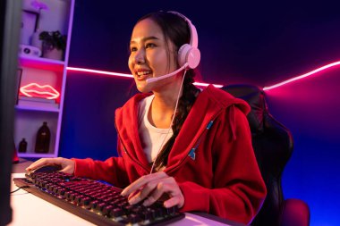 İnternet üzerinden kulaklık takıp gülümseyen Asyalı güzel kız flamasının sunucu kanalı izleyicilerle internet üzerinden konuşma yapıyor. Esport yetenekli takım oyuncuları neon mavi odada. Taktik.