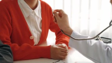 Hasta klinikte ya da hastane ofisinde doktor randevusuna gidiyor. Hastaların nabzını steteskopla kontrol edip risk faktörünü belirleyen doktor semptomları inceliyor. Panorama. Katı.