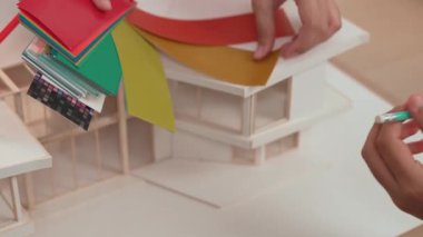 Mimari ekipman kullanarak yavaş çekim ev tasarımcısı bir plan çizerken, iç mimari tasarımcı da müşterilerin talebine göre renk örneklerinden uygun renkler seçiyor. Değiştirilmiş
