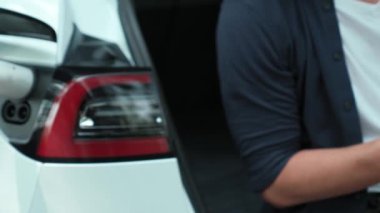 Ulusal Park veya Yaz Ormanı 'ndaki tatil gezisi sırasında EV şarj istasyonundan elektrik aküsü almak için akıllı telefon internet bankacılık uygulaması kullanan bir adam. Yükselt