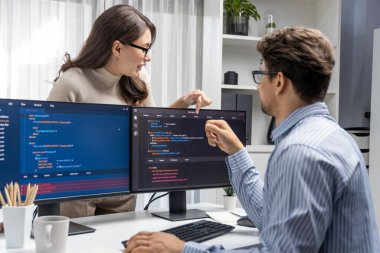 Masada çalışan erkek programcının karşısında duran kadın meslektaşım iki bilgisayar ekranında kodlama web sitesi yazılım sistemi projesini tartışmak için tam yığın veri dizaynı ile karşılaştırıyor. Varsayım.