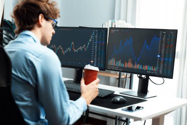 İki ekranda piyasa grafiği verilerine odaklanan ve elinde modern ofiste arka manzaralı kahve fincanı tutan genç bir tüccar. Dinamik para bozdurma oranını analiz etme kavramı. Toplayıcı.