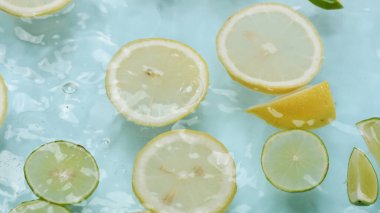 Dilimlenmiş limon makrosu, limon ve limonla suya dökülüyor. Mavi arka planda yüzüyor. Citrus meyve hareketi berrak suda ilerliyor. Citrus tazeliği. Tazelik ve susuzluk kavramı. Pabulum.
