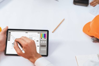 Mimari proje üzerinde birlikte çalışan çeşitli inşaat mühendisi ve müvekkil grupları, toplantı masasında tablet kullanarak inşaat planını gözden geçirip bina planı hazırlıyorlar. Tedbirli