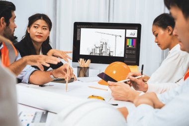 Mimari proje üzerinde birlikte çalışan çeşitli inşaat mühendisi ve müvekkil grupları, inşaat planını gözden geçirip toplantı masasında plan oluşturuyorlar. Tedbirli