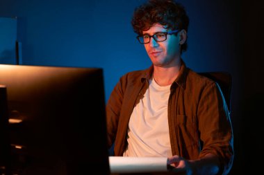 Genç işadamı, Neon Light Modern Ofis 'teki yeni proje surround çalışma masası için kağıt üzerinde tasarım düşünüyor. E-posta ile hediye göndermeden önce not defterine yeni bir iş düşünüyorum. Toplayıcı.