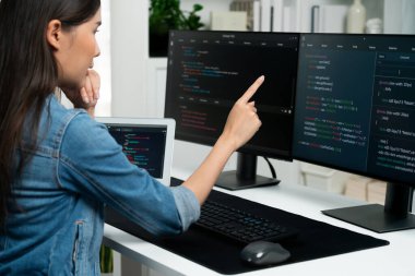 İnternet sitesinde kodlama programı uygulaması olan ve kot gömlek giyen bilgisayar hakkında bilgi veren IT geliştiricisi genç bir Asyalı kız. Güvenlik programlarıyla çevrili iki ekran. Taktik.