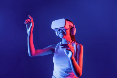 Siberpunk neon ışığı altında duran zeki kadın metaevrene bağlı VR kulaklık takıyor, gelecekçi siber uzay topluluğu teknolojisi. Zarif bir kadın parmak ucu kullanarak sanal bir obje oluşturur. Halüsinasyon.