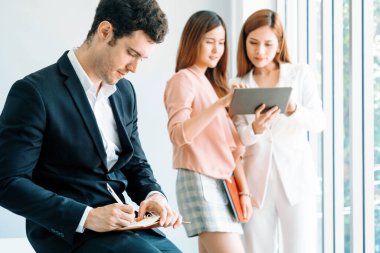 Kitap okuyan ve iş yerinde iş arkadaşları ve arkadaşlarıyla çalışan genç ve yakışıklı bir işadamı. Kurumsal iş adamları grubu. uds