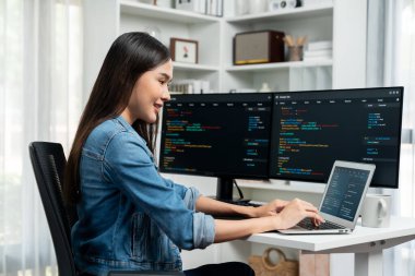 IT geliştiricisinde gülümseyen genç Asyalı dizüstü bilgisayarında kodlama programı verileriyle kotlu tişört giyerek çevrimiçi bilgi yazıyor. Güvenlik analizi iki ekran ile çevrili. Taktik.