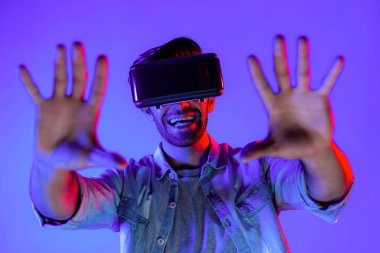 Heyecan verici bir sporcu el hareketi yaparken VR gözlüğü takıyor. Yetenekli genç ayakta duruyor ve teknolojik yenilikleri kullanarak gelecekteki sanal dünya programını veya metaevreni inceliyor. Sapma.